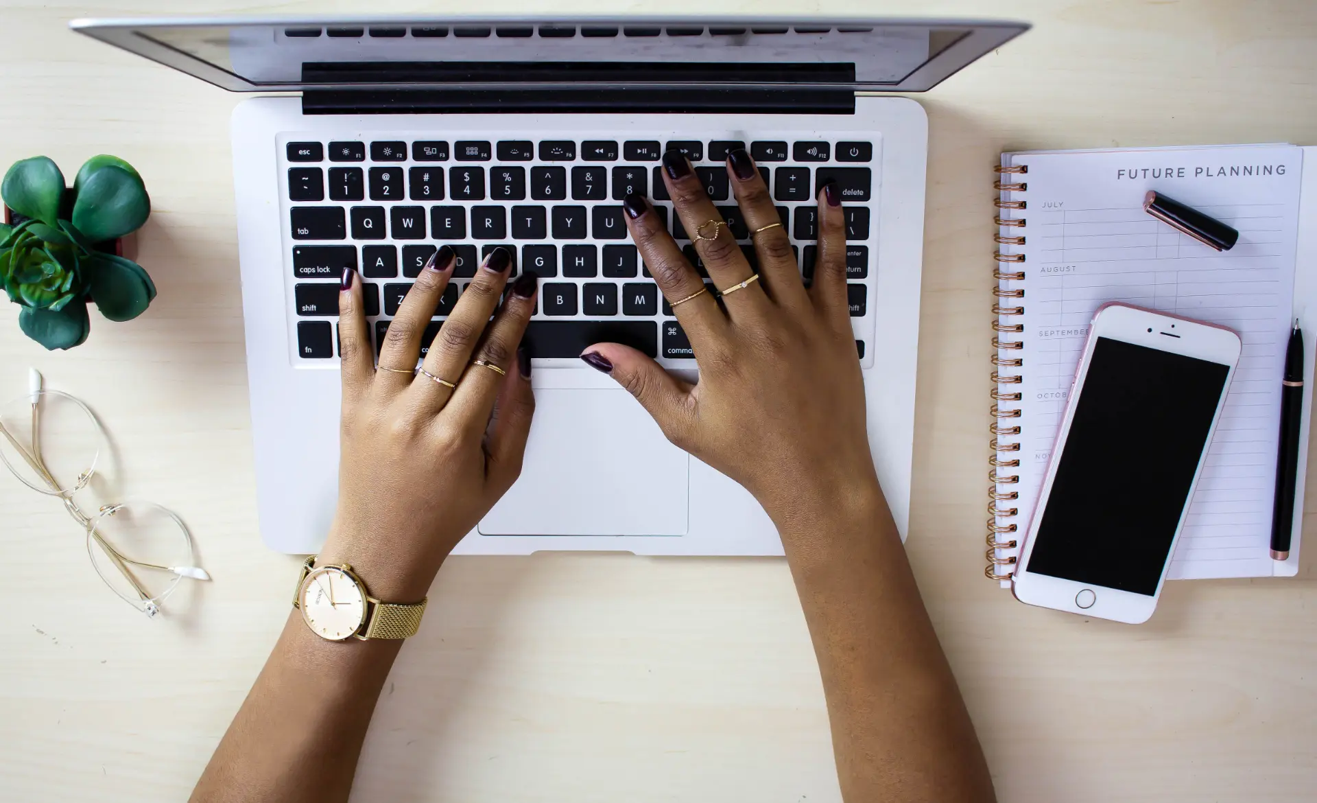 A workspace flat-lay with a laptop, planner, and desk accessories